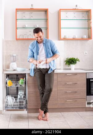 Young man in kitchen doing chores cleaning wiping dishes. Attractive man polishing plate smiling happy. Stock Photo