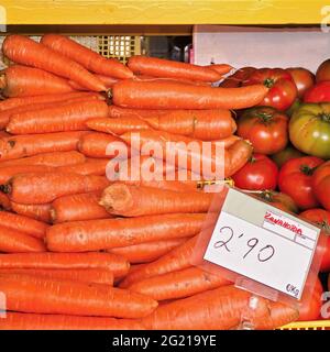 Fresh carrots piled on top of each other for sale at an outdoor market stall. Next door there are still tomatoes in green and red. Close-up in the fro Stock Photo