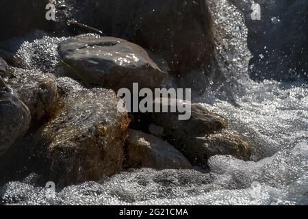 The chaos of a fresh clear mountain creek flowing over sunny rocks while splashing water drops and creating bubbles, Tirol, Austria Stock Photo