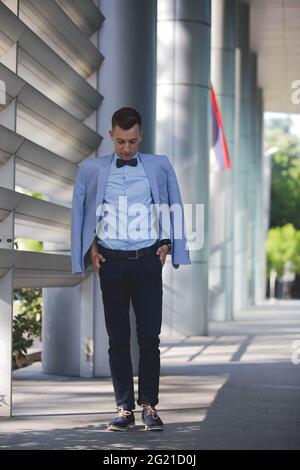 Young stylish man standing with hands in pocket and jacket on his shoulders Stock Photo
