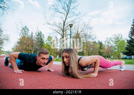 Shot of healthy young couple doing stretching exercises together on green meadow in the morning Stock Photo