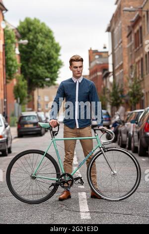 Handsome caucasian man in fashionable outfit posing with a trendy vintage bicycle on the street of Shoreditch , London. Stock Photo