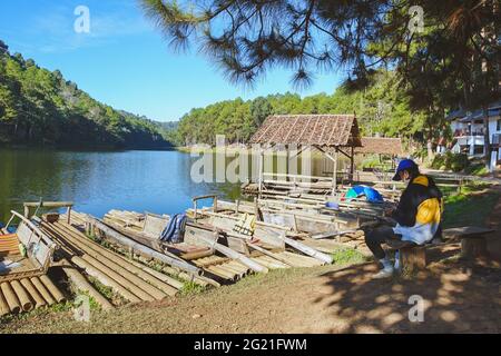 Mae Hong Son, Thailand - December 15, 2020: service worker of  Pang Oung raft is sitting under a pine tree at Pang Oung Reservoir. Stock Photo