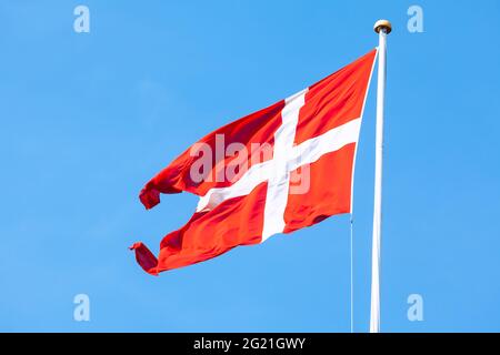 Waving flag of Denmark against blue sky . Red flag with white cross