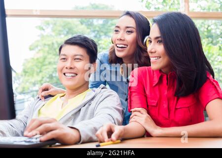 Three young and creative enthusiastic colleagues looking at the monitor of a desktop PC while working together on a project Stock Photo