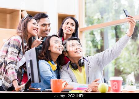 Creative team of five enthusiastic employees making a selfie photo with the mobile phone in the office Stock Photo