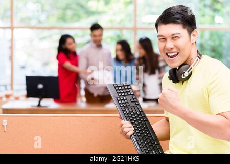 Portrait of young Chinese employee happy for his successful work on computer and for his contribution to the success of the team Stock Photo