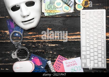 Composition with mask, PC keyboard, handcuffs and money on wooden background. Hacking concept Stock Photo