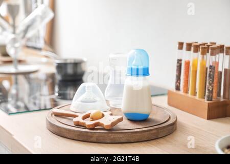 Bottles of milk for baby with rattle on table in kitchen Stock Photo