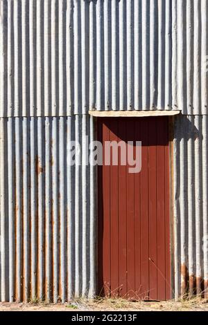A rust red wooden door in a rusty silver corrugated iron wall with copy space. Stock Photo