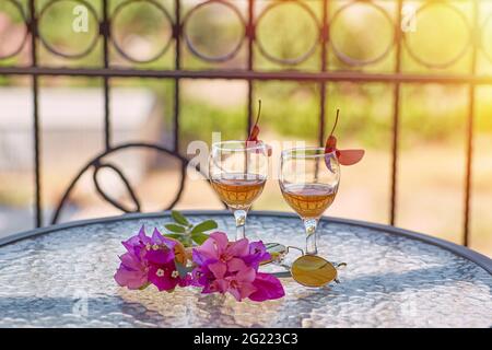 Glasses with homemade liqueur, decorative with fresh summer surreal flowers. Summer bright background for advertising cocktails and relaxation. High quality photo  Stock Photo