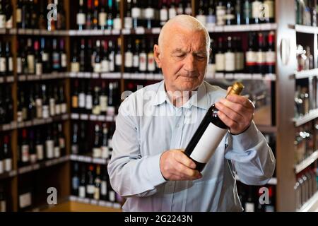 Elderly man chooses red wine in a liquor store Stock Photo