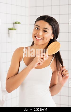 young african american woman brushing hair and looking at camera in bathroom Stock Photo