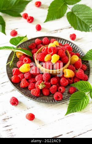 Ripe juicy sweet berries of yellow and red raspberries on a white rustic table. Stock Photo