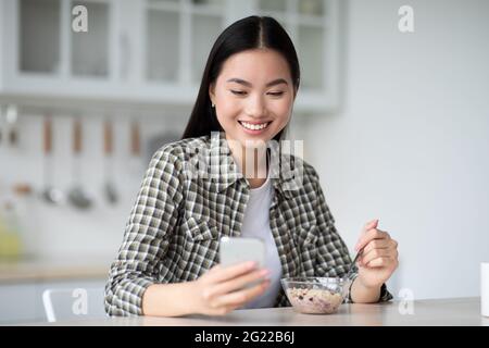 Smiling asian woman surfing on Internet while having breakfast Stock Photo