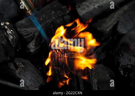 Burning charcoal close up. Coal lump on gas flame. Camp fireplace fuel for meat cooking. Natural dark mineral, burnt texture. Fire glowing object Stock Photo