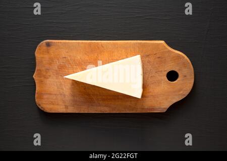 Pecorino Romano Cheese on a rustic wooden board on a black surface, top view. Flat lay, overhead, from above. Stock Photo