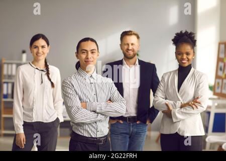 Happy businessman with team of loyal employees standing in office and smiling at camera Stock Photo