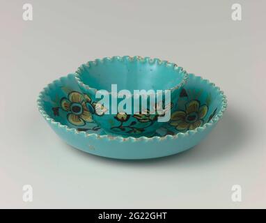 Dish. Dish of multicolored painted faience. The cup and saucer are painted with yellow flowers on a turquoise background. The edges of the dish are serrated. Stock Photo