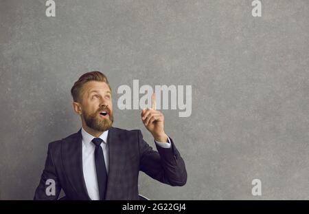 Young businessman looking and pointing up against grey copy space studio background Stock Photo