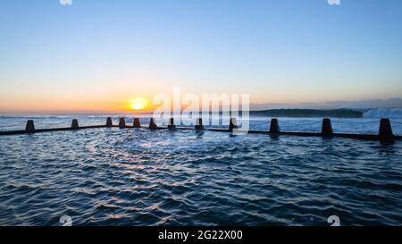 Beach tidal swimming pool with large ocean waves crashing breaking at dawn sunrise on the horizon. Stock Photo