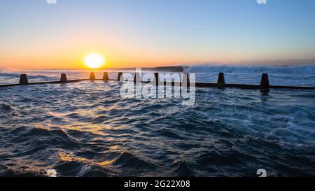 Beach tidal swimming pool with large ocean waves crashing breaking at dawn sunrise on the horizon. Stock Photo