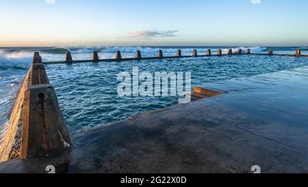 Beach tidal swimming pool with large ocean waves crashing breaking at dawn sunrise on the horizon. Stock Photo