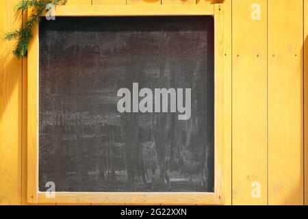 Empty space concept for advertising, mockup. Front view of a blank blackboard for text with Christmas tree branches and wooden surface in background. Stock Photo