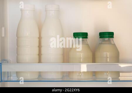 Fermented kefir in refrigerator. White dairy products in plastic bottles on shelf of open empty fridge. Horizontal view. Stock Photo