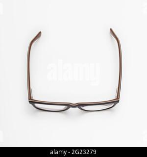 A pair of dark blue and brown eyeglasses with open temples placed on a white surface, viewed from above Stock Photo