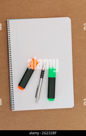 Notebook with grid sheets on which there are two markers and a pen and which is placed on a cardboard surface. The orientation of the image is vertica Stock Photo