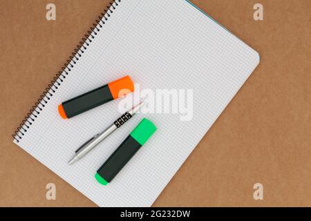 Notebook with grid sheets on which there are two markers and a pen and which is placed on a cardboard surface. The orientation of the image is horizon Stock Photo