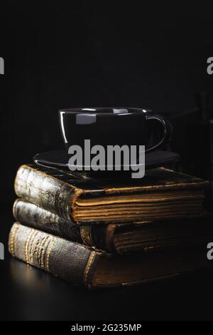 Coffee mug and antique books on black table. Stock Photo