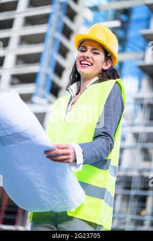 Female architect studying drafts while visiting large construction site Stock Photo