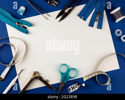 Sewing tools on a blue background with copy space. Scissors, sewing threads, centimeter, thimble, zippers, nippers and other supplies. Top view Stock Photo