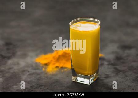 Turmeric latte, a golden milky hot healthy drink on a dark background in a glass tumbler Stock Photo