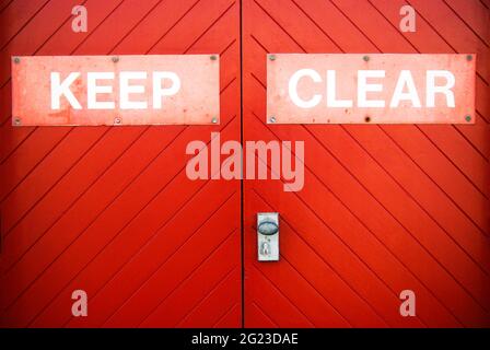Keep Clear sign painted on a bright red wooden garage doors to stop people from blocking access. Stock Photo