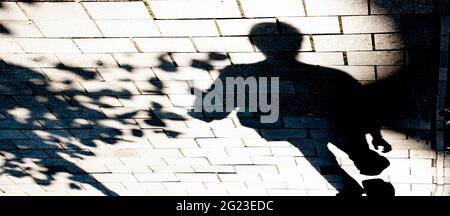 Blurry shadow silhouette of a person walking city street sidewalk on sunny summer day, in black and white Stock Photo