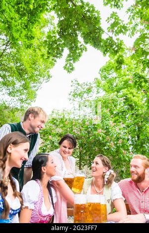 Waitress in beer garden serving drinks to three women and man Stock Photo