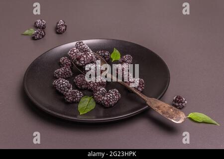 Blackberries on a ceramic plate. Frozen fruits for a healthy food diet. Minimalistic concept, black stone concrete background, flat lay
