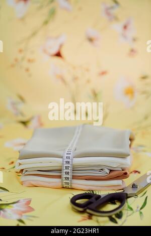 Tailor gift card holiday concept. Fabrics in stack folded as a present with beautiful ribbon using measure tape and sharp tailors scissors near it. Gift for dressmaker. High quality vertical photo Stock Photo