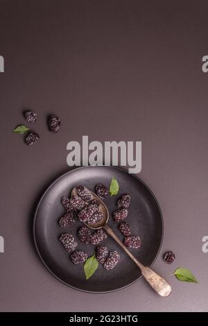Blackberries on a ceramic plate. Frozen fruits for a healthy food diet. Minimalistic concept, black stone concrete background, top view