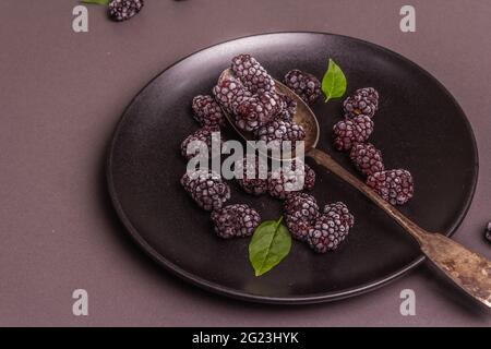 Blackberries on a ceramic plate. Frozen fruits for a healthy food diet. Minimalistic concept, black stone concrete background, flat lay
