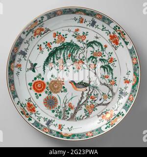 Saucer-Dish With Flower Sprays, Birds and Insects. Dish of porcelain with round wall, painted in underglaze blue and on the glaze blue, red, green, yellow, eggplant, black and gold. On the flat a chrysanthemum and a flowering tree, a bird on a willow branch, a butterfly and insect in the air; Four times a ponda branch on the wall; The edge with a fish or shrimp in a cartouche interspersed with stylized lotus branches against a black dotted green soil; the back with four flower branches; On the edge a bond with fish in cartouches and half chrysanthemums interspersed with napkin. A double circle Stock Photo