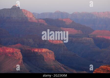The day ends as the sun accentuates the shapes and saturates the reddish colors of the South Rim Mountains in Grand Canyon National Park, Arizona. Stock Photo
