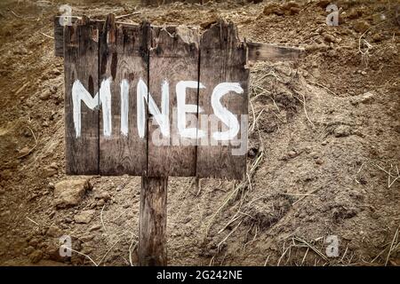 Wooden weathered warning sign for mines in front of a minefield Stock Photo