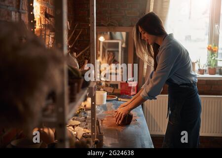 Charming young lady hanging out in pottery workshop while working with fresh clay Stock Photo