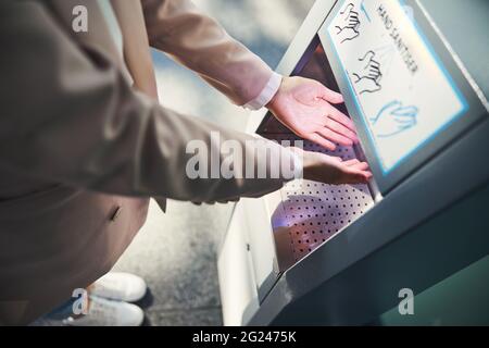Female person using automatic hand sanitizer at airport Stock Photo