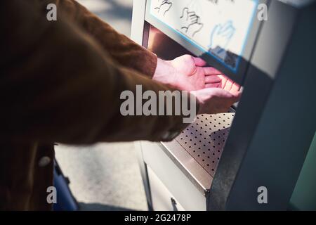 Young man using automatic hand sanitizer at airport Stock Photo