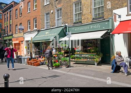 Woman wearing face mask and person looking at plants in Exmouth Market street in Clerkenwell row flats above shops London EC1 England UK  KATHY DEWITT Stock Photo